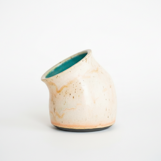 Small ceramic vase with a textured beige exterior and teal interior on a white background